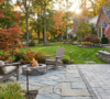 A luxury backyard patio design in East Amherst, NY, showcasing a side-by-side comparison of organic natural stone flagstone surrounding a stone fire pit next to smooth, geometric interlocking concrete pavers.