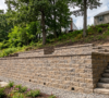 A professionally engineered multi-tiered concrete block retaining wall with built-in stone steps terracing a steep sloped backyard in Amherst, NY.