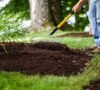 Landscaper spreading a fresh layer of dark organic bark mulch on a residential garden bed in Amherst NY