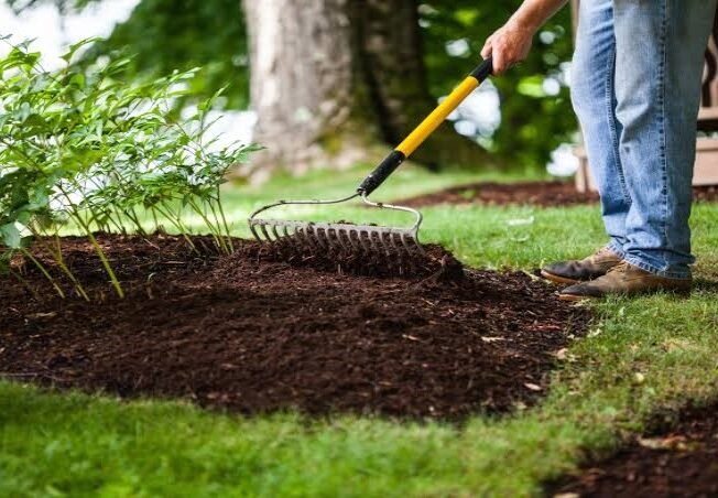 Landscaper spreading a fresh layer of dark organic bark mulch on a residential garden bed in Amherst NY