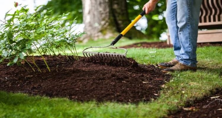 Landscaper spreading a fresh layer of dark organic bark mulch on a residential garden bed in Amherst NY