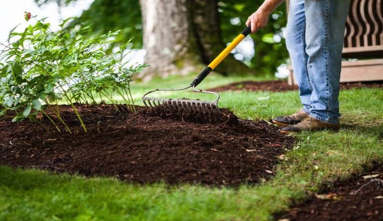 Landscaper spreading a fresh layer of dark organic bark mulch on a residential garden bed in Amherst NY